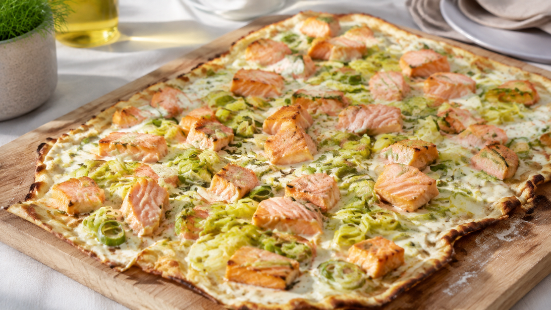 Dünner gegrillter Flammkuchen mit unterschiedlich großen Lachsstücken und Lauchringen