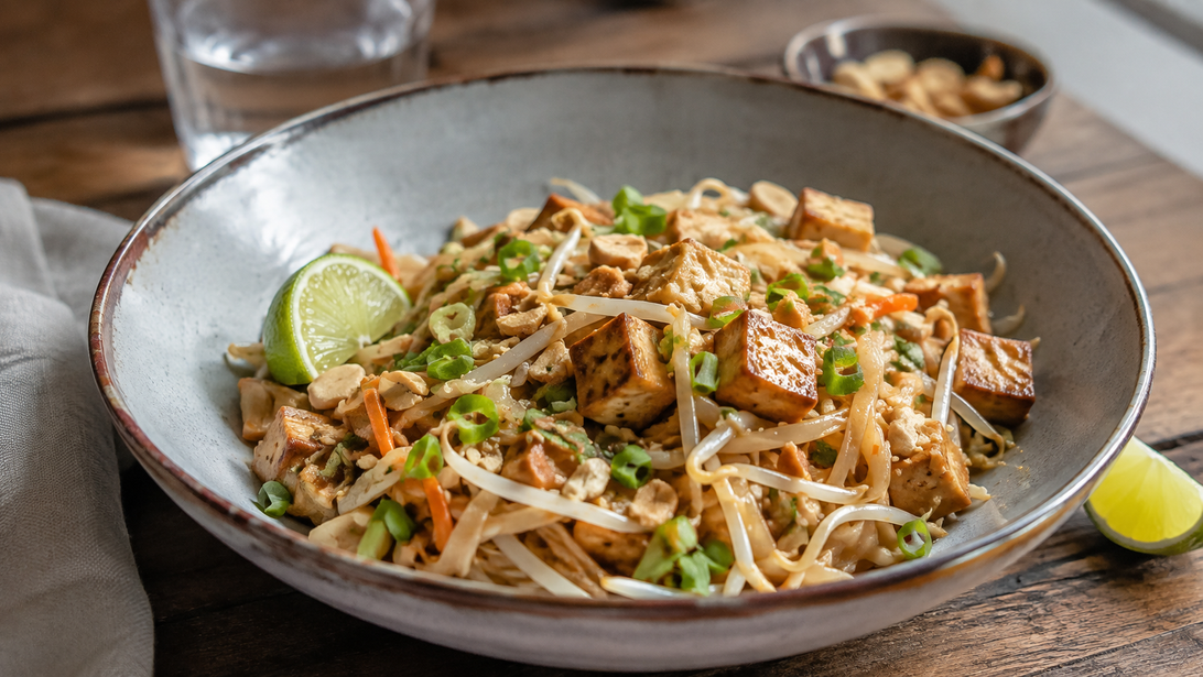 Gebratene Reisnudeln mit goldbraunem Tofu, Sprossen, Karotte, Erdnüssen und Limette